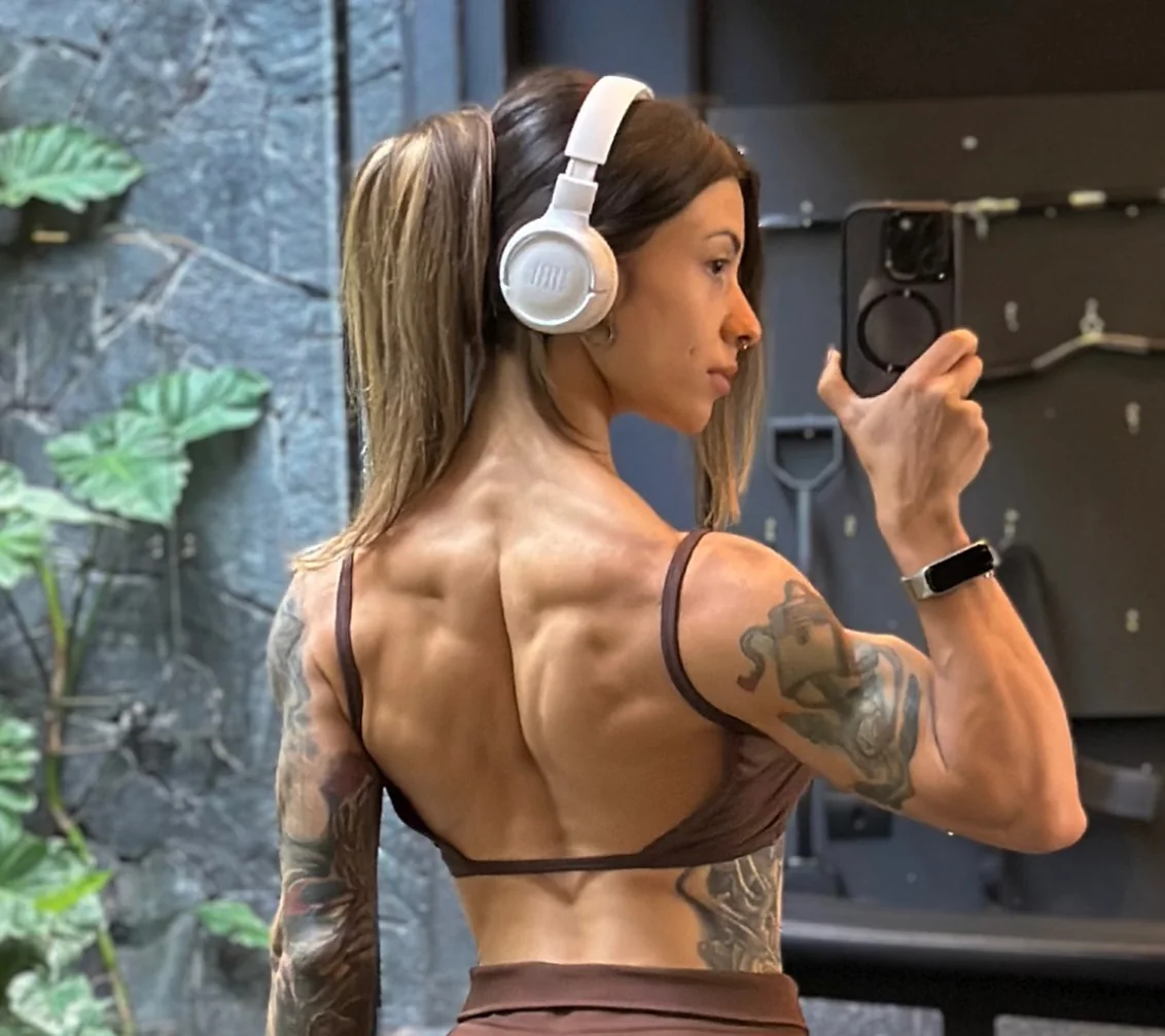 Bianca Mattos de costas em selfie de espelho, com fones brancos, mostrando as costas e o braço tatuado