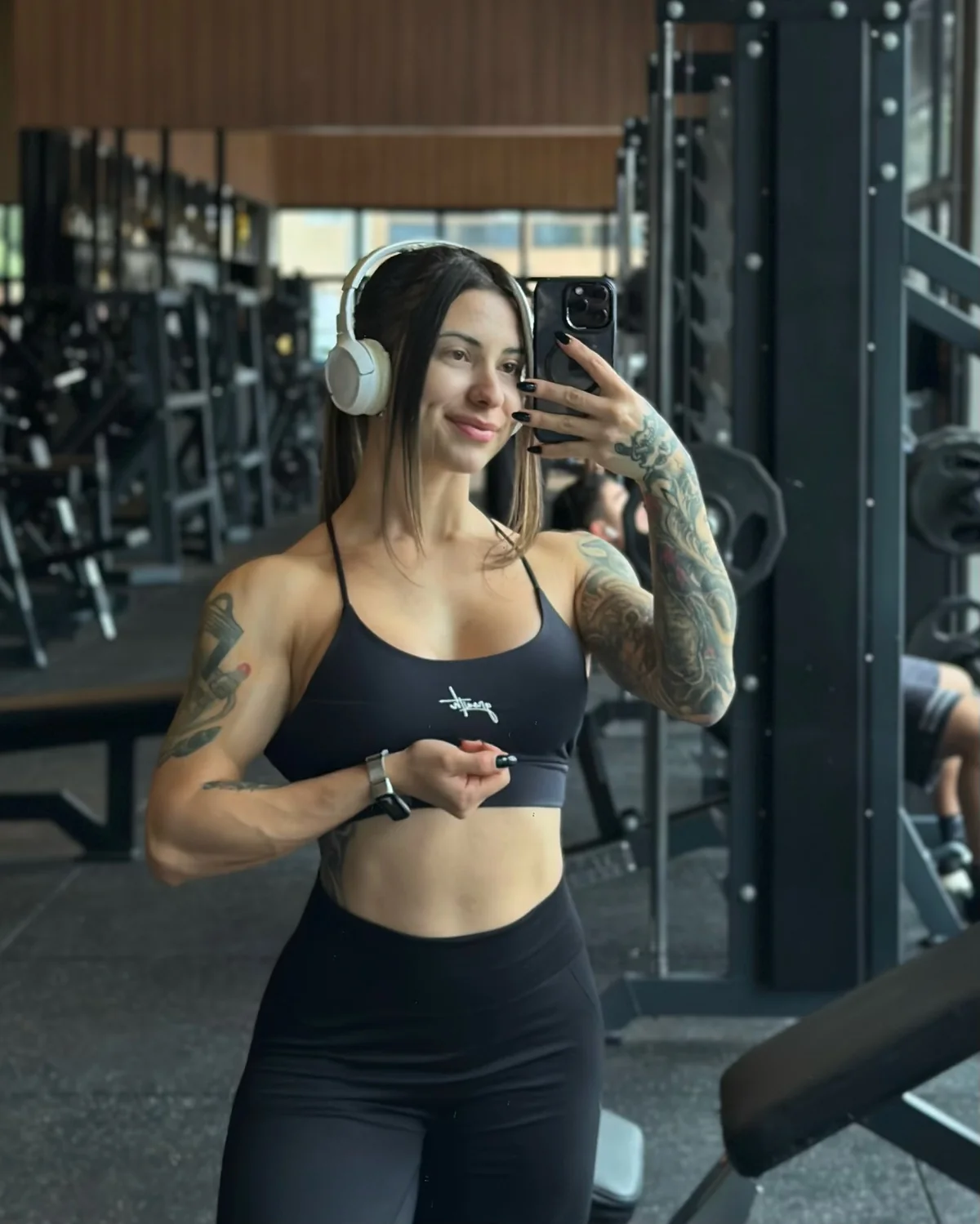 Bianca Mattos em selfie de espelho na academia, de top preto, com fones de ouvido